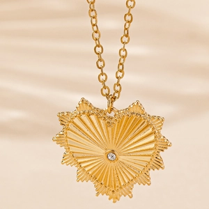 Golden heart pendant necklace with sunburst engraving and crystal on beige satin