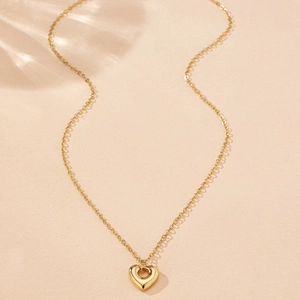 Détails d'un collier doré avec pendentif cœur ajouré et chaîne croisée élégante