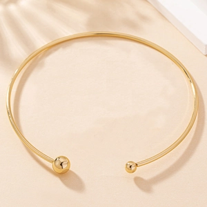 Detail of minimalist gold torque necklace with polished bead ends on beige background