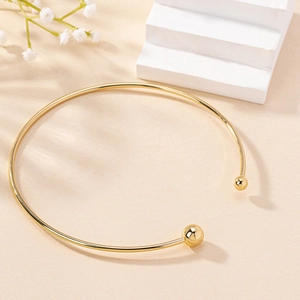 Minimalist gold open collar necklace with polished metal beads on an elegant display