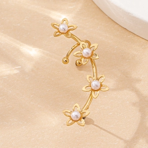 Détail d'un ear cuff doré orné de motifs floraux et de perles blanches élégantes
