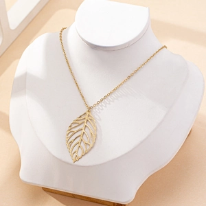 Collier élégant avec pendentif feuille évidée dorée sur présentoir avec ombres douces