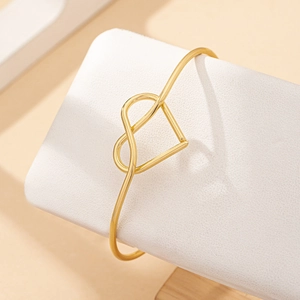 Elegant gold-tone bangle featuring a hollow heart-shaped knot on a textured display stand