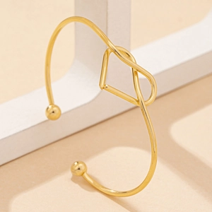 Minimalist gold heart-shaped open cuff bracelet on white geometric stand