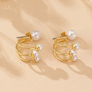 Detailed view of layered C-shaped gold stud earrings with white pearl accents