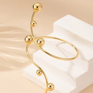 Fashionable gold spiral bracelet with polished metal beads on minimalist tiered display