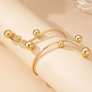 Artistic gold beaded open bangle bracelet with a minimalist branch design on a beige stand