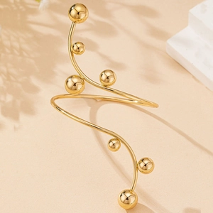 Detail view of a gold spiral arm cuff with polished spheres on a warm beige background