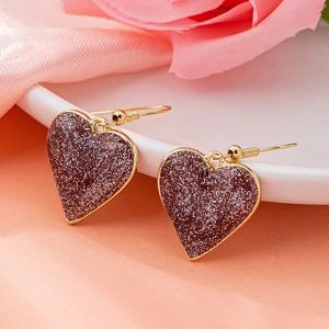 Close-up of heart-shaped glitter earrings with gold hooks on elegant pink silk background