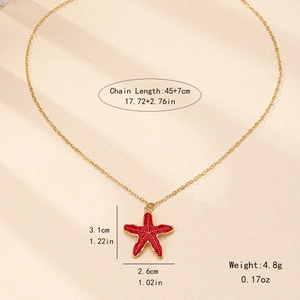 Elegant gold chain necklace with a red enamel starfish pendant on sandy beach background