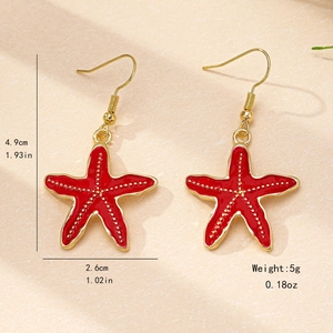 Boucles d'oreilles étoiles de mer en émail rouge avec détails dorés sur fond beige