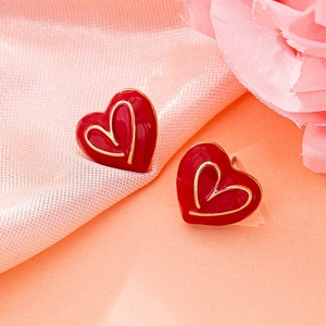 Vue détaillée des boucles d'oreilles cœur rouge bordées d'or sur satin rose