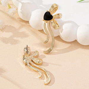 Elegant gold earrings featuring black heart charms and fluid metal ribbons on sand