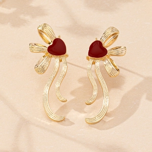 Detail of elegant gold heart earrings with textured ribbon design on beige surface