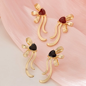 Elegant gold earrings with red and black enamel hearts on flowing silk ribbon background