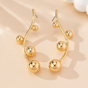 Detail of elegant gold curved branch earrings with polished metal beads on stone surface