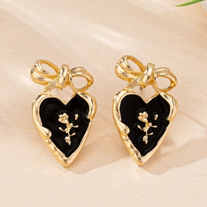 Detailed close-up of heart earrings with black enamel, gold bow, and rose embossing
