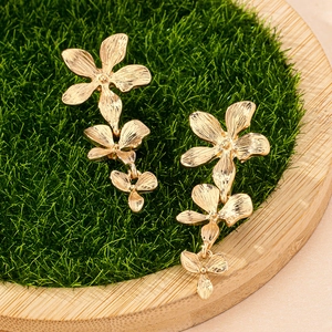 Eleganti orecchini pendenti a fiore dorati con trama in metallo spazzolato su verde