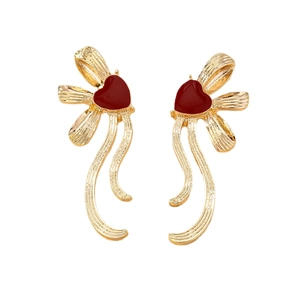 Elegant gold ribbon bow earrings with red heart pendants in textured metallic finish