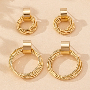 Detailed view of layered golden geometric hoop earrings on a textured beige surface
