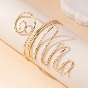 Macro detail of golden spiral arm cuff with diamond-cut texture on a white display