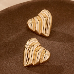 Elegant gold heart stud earrings with textured spiral design on brown background