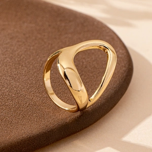 Close-up of golden irregular cutout ring on a textured dark pedestal with soft lighting