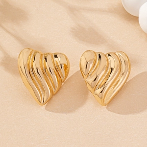 Close-up of golden heart earrings featuring vertical pleated texture and metallic finish