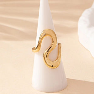 Modern gold irregular wave ring with an abstract curved design on a white cone stand