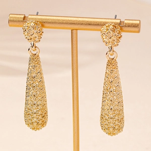 Détail de longues boucles d'oreilles goutte d'or avec finition mate texturée