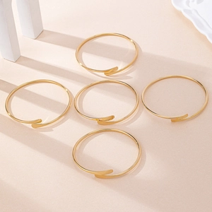 Vue détaillée de cinq bracelets joncs dorés minimalistes empilés sur un fond beige mat