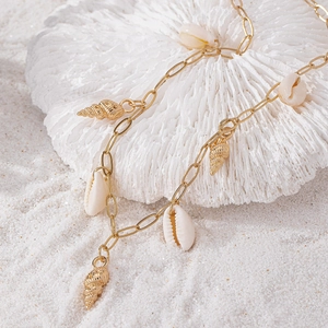 Elegant gold chain necklace with natural white shells and spiral charms on coral sand