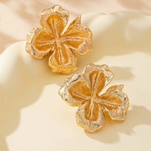 Elegant gold flower stud earrings with brushed texture on minimalist display dish