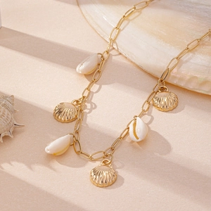 Vue détaillée du collier coquillage doré avec pendentifs naturels sur fond de sable fin
