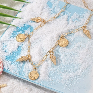 Gold ocean style chunky necklace with shell and conch pendants on beach sand background