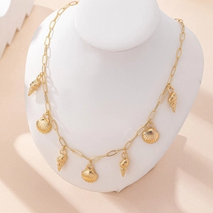 Gold ocean style necklace with seashell and conch pendants on white display stand