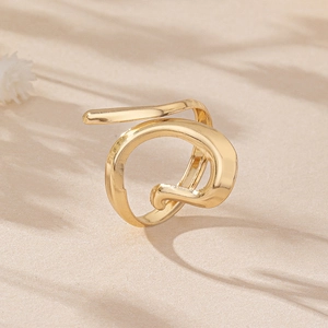 Detailed close-up of golden irregular flowing ring on a minimalist sandy background