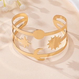 Detail of gold hollow open cuff bracelet with sun moon and star motifs on sandy background