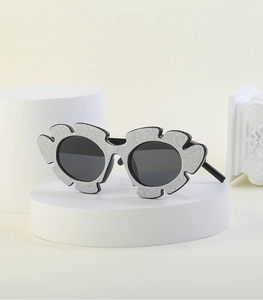 Detail of silver glitter flower sunglasses with grey round lenses on a white platform