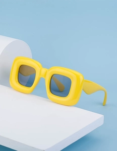 Detail of trendy yellow square sunglasses on a white geometric block against blue background