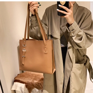 Detail view of large brown PU leather tote bag with silver metal ring buckle held by model