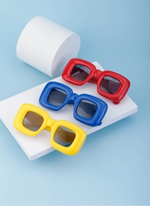 Three pairs of thick square frame sunglasses in red blue and yellow on white blocks