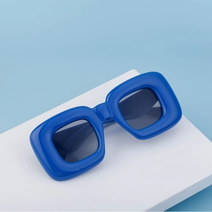 Detailed side view of bold square royal blue sunglasses on a white podium