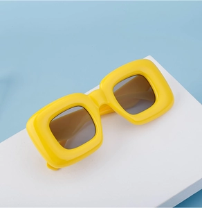 Close-up of chunky square yellow sunglasses on a geometric block against blue backdrop