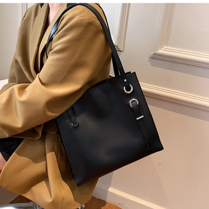 Detail of black leather tote bag with silver eyelets and side buckle on a shoulder strap