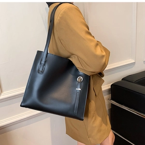 Close-up of minimalist black leather tote bag with silver ring and long shoulder straps