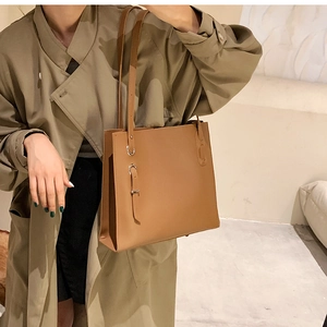 Brown faux leather tote bag with side buckle detail shown on a model in a trench coat