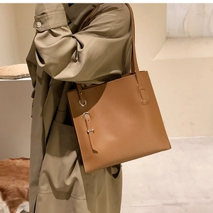 Detailed view of caramel brown leather tote bag with silver buckle worn with a dark coat