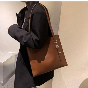Brown leather tote bag featuring silver eyelets and buckle strap worn by a model