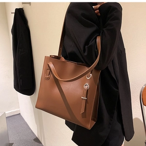 Side view of a large brown leather tote bag with metal ring detail on a black blazer model